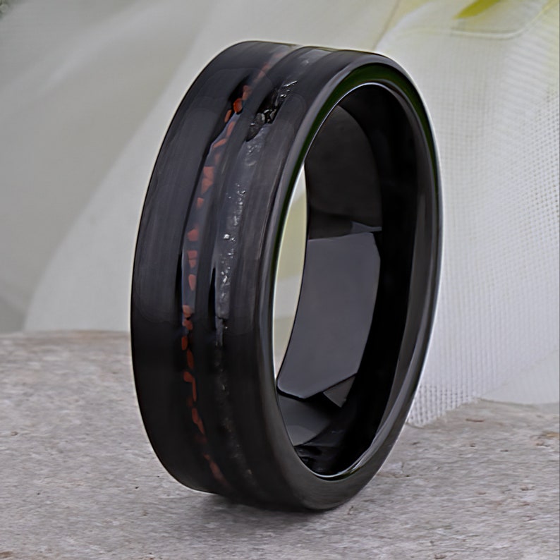 May include: A black tungsten carbide ring with a red and black inlay. The ring has a polished finish.