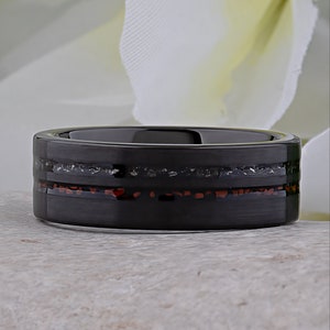 May include: A black tungsten carbide ring with a thin red and silver inlay. The ring has a brushed finish.