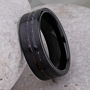 May include: A black tungsten carbide ring with a red and gray inlay. The ring has a polished finish and a beveled edge.