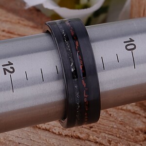 May include: A black and red ring with a textured finish. The ring is on a metal sizing tool, with the numbers 10 and 12 visible.
