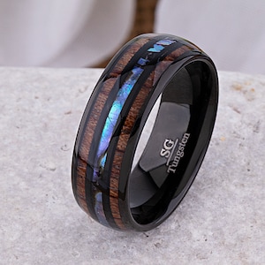 May include: Black tungsten ring with a brown wood inlay and a blue abalone shell inlay. The ring is engraved with "SG Tungsten".