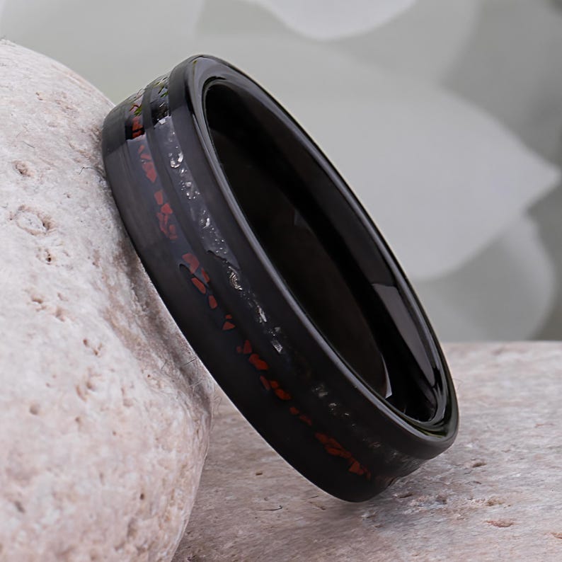 May include: A black tungsten carbide ring with a red and black inlay. The ring is polished and has a smooth finish.