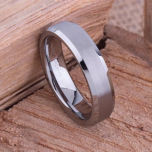 May include: A silver tungsten carbide ring with a bevelled edge and a brushed finish.