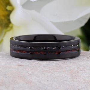 May include: A black tungsten carbide ring with a red and silver inlay. The ring has a brushed finish.