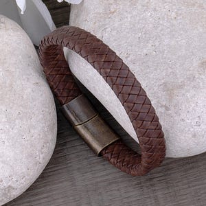 Peut inclure: Un bracelet en cuir marron avec un design tressé et un fermoir en métal.