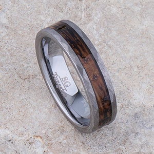 Puede incluir: Un anillo de tungsteno plateado con una incrustación de madera marrón y un acabado martillado. El anillo está grabado con "SG Tungsten".
