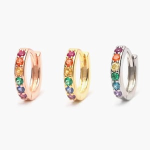 May include: Three pairs of rainbow hoop earrings. The earrings are made of silver, gold, and rose gold. Each earring has a row of colourful gemstones.