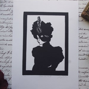 Pode incluir: Impressão em preto e branco de uma mulher em perfil, usando um chapéu grande com uma pena e um broche. A obra de arte é emoldurada em uma borda preta e colocada em um fundo de escrita antiga e elementos decorativos.