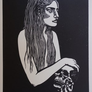 Puede incluir: Grabado en lin&oacute;leo en blanco y negro que representa a una mujer con pelo largo sosteniendo una calavera. La obra est&aacute; firmada y numerada 1/30. La impresi&oacute;n tiene un estilo minimalista con alto contraste.