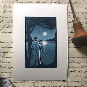 Peut inclure: Une estampe bleue et blanche représente une personne contemplant un lac éclairé par la lune. L'œuvre, encadrée en blanc, montre une silhouette en manteau, près d'un arbre, sur fond de ciel bleu foncé.