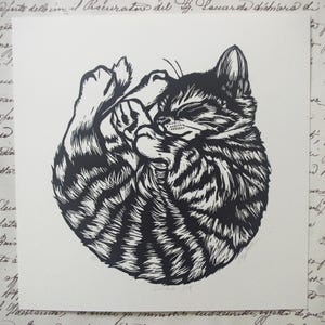 Peut inclure: Impression en noir et blanc d'un chat endormi enroulé en boule. Le chat a des rayures et est dessiné dans un style réaliste.