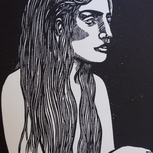 Puede incluir: Un grabado en lin&oacute;leo en blanco y negro de una mujer con cabello largo y suelto. La mujer est&aacute; representada de perfil, con un trabajo de l&iacute;nea detallado que define sus rasgos y cabello. El fondo es negro s&oacute;lido, creando un fuerte contraste.