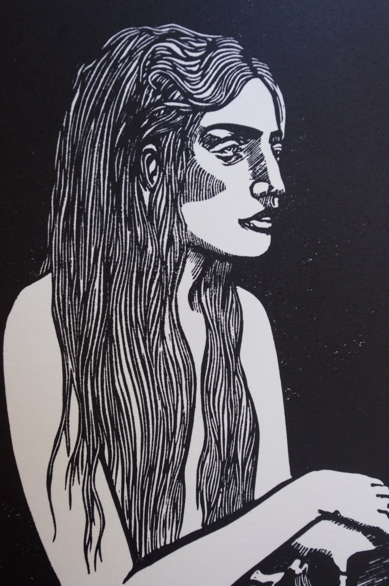 Puede incluir: Un grabado en lin&oacute;leo en blanco y negro de una mujer con cabello largo y suelto. La mujer est&aacute; representada de perfil, con un trabajo de l&iacute;nea detallado que define sus rasgos y cabello. El fondo es negro s&oacute;lido, creando un fuerte contraste.