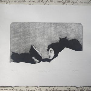 Peut inclure: Une gravure en noir et blanc sur papier texturé représentant une personne lisant un livre en position allongée. Deux chats sont placés près de la personne, l'un reposant sur l'épaule et l'autre près des mains. L'œuvre est centrée sur un fond d'écriture cursive.