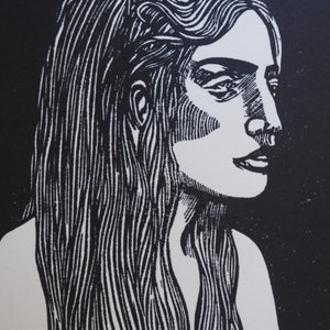 Puede incluir: Un grabado en lin&oacute;leo en blanco y negro que muestra el perfil de una mujer. La obra de arte presenta una representaci&oacute;n detallada de una mujer con cabello largo y suelto. La imagen es un estudio de contrastes, con la figura blanca sobre un fondo negro.