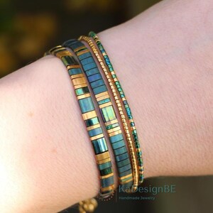 May include: Three bracelets on a wrist. The bracelets are teal and gold. The first bracelet is made of rectangular teal and gold beads. The second bracelet is made of small teal beads. The third bracelet is made of small gold beads.