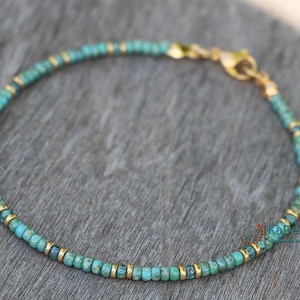May include: A turquoise and gold beaded bracelet with a clasp closure. The bracelet is made with small, round beads and is delicate in appearance.