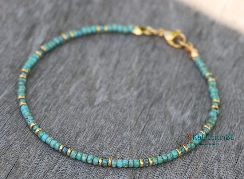 May include: A turquoise and gold beaded bracelet with a clasp closure. The bracelet is made with small, round beads and is delicate in appearance.
