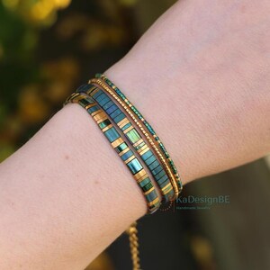 May include: A close-up of three bracelets on a wrist. The bracelets are teal, gold, and green. The first bracelet is made of rectangular teal beads with gold accents. The second is a thin gold chain. The third is made of small green beads. The text "KaDesignBE Handmade Jewelry" is visible.