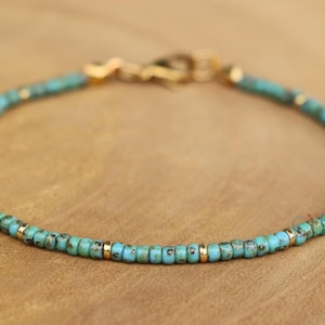 K&ouml;nnte beinhalten: Ein t&uuml;rkisfarbenes und goldenes Armband mit einem Karabinerverschluss.