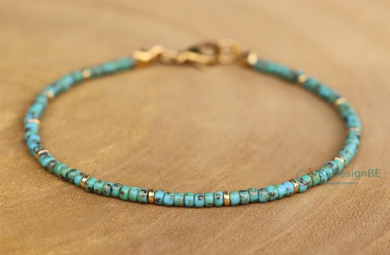 K&ouml;nnte beinhalten: Ein t&uuml;rkisfarbenes und goldenes Armband mit einem Karabinerverschluss.