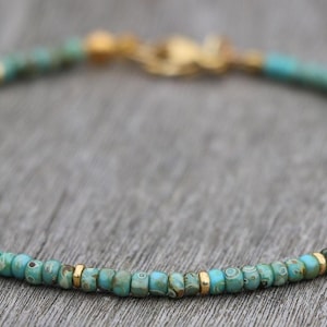 K&ouml;nnte beinhalten: Ein t&uuml;rkisfarbenes und goldenes Armband mit einem zarten Kettenverschluss.