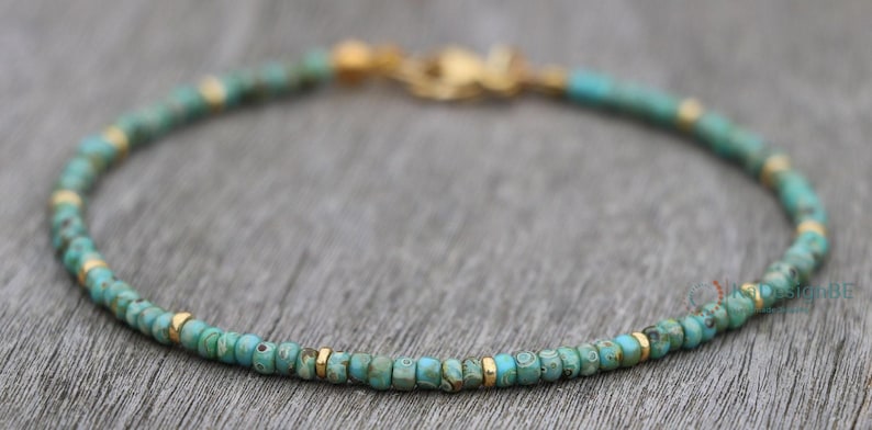K&ouml;nnte beinhalten: Ein t&uuml;rkisfarbenes und goldenes Armband mit einem zarten Kettenverschluss.