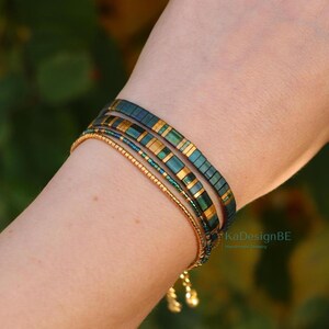 May include: A set of four bracelets in shades of gold, teal, and dark blue. The bracelets are worn on a wrist. The top two bracelets have a rectangular design with gold accents. The bottom two bracelets are made of small beads. The text "KaDesignBE" is visible.