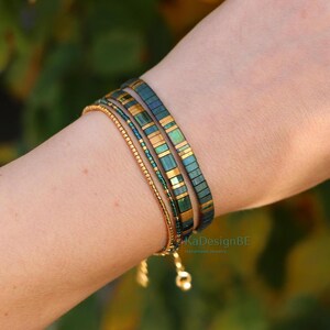 May include: A collection of handmade bracelets. The bracelets include a gold chain bracelet and two dark teal and gold beaded bracelets. The bracelets are stacked on top of each other. The bracelets are on a person's arm.
