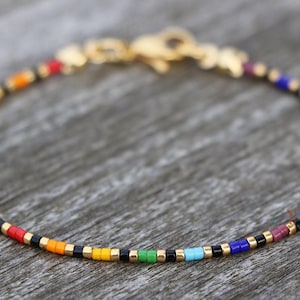 Peut inclure: Un bracelet en perles colorées avec des perles noires et dorées. Le bracelet est composé de petites perles carrées dans un motif arc-en-ciel.
