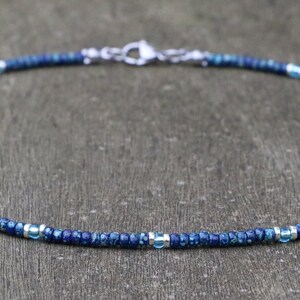 blue seed bead necklace on wooden surface. pattern: 12 blue beads, 1 aqua beads, 12 blue beads, 1 aqua bead...   around the aqua bead there are silver spacers. stainless steel lobster clasp. minimalist boho style. good layering with blue or silver