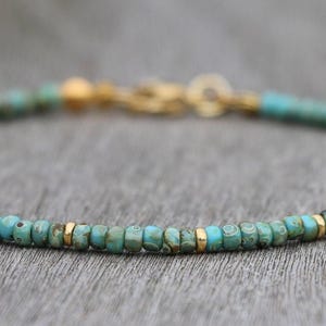 K&ouml;nnte beinhalten: Ein t&uuml;rkisfarbenes Armband mit goldenen Perlen. Das Armband besteht aus kleinen, runden t&uuml;rkisfarbenen Perlen und goldenen Zwischenst&uuml;cken.