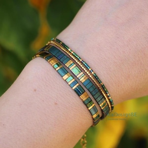 May include: A set of four bracelets in shades of teal, gold, and green. The bracelets are worn on a wrist and feature a mix of rectangular and beaded designs. The bracelets have a delicate and elegant appearance.