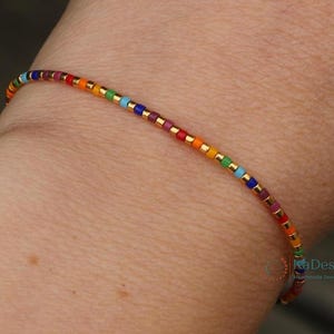 Può includere: Un braccialetto di perline colorate con un arcobaleno di colori, tra cui rosso, arancione, giallo, verde, blu e viola. Il braccialetto ha distanziatori color oro tra le perline. Gioielli fatti a mano.