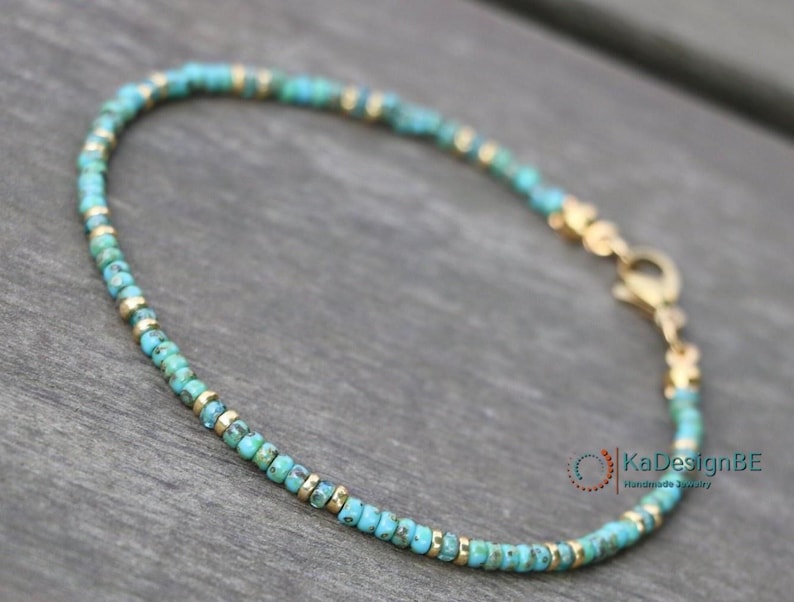 May include: A delicate turquoise and gold beaded bracelet with a lobster clasp closure. The bracelet is handmade and features small, round beads.