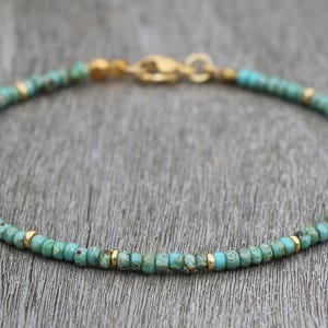 Może przedstawiać: Bransoletka z turkusowych i złotych koralików z zapięciem.