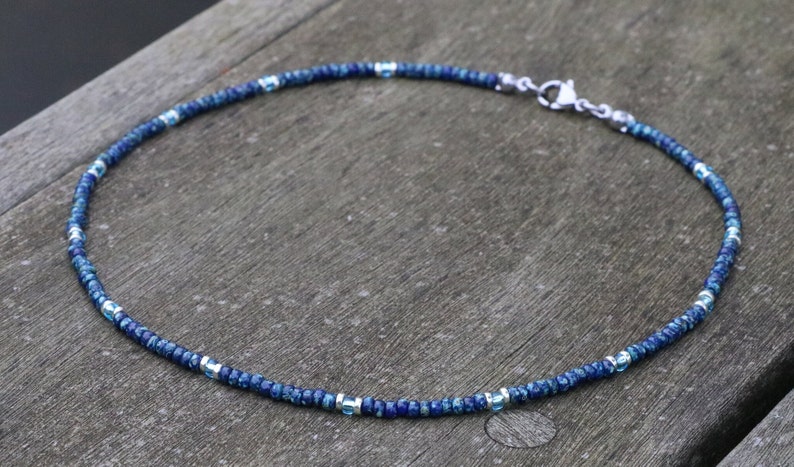 Blue seed bead necklace on wooden surface. every 12 blue picasso beads, there is an aqua bead surrounded by silver spacers. dainty bohemian jewelry style.lightweight. perfect as summerbeach jewelry