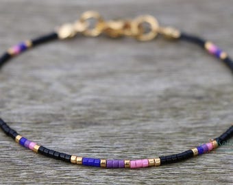 Könnte beinhalten: Ein zartes Armband mit schwarzen, rosa und violetten Perlen. Das Armband hat einen goldenen Verschluss.