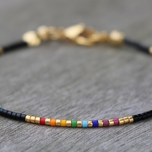 May include: A delicate bracelet with black beads and a rainbow of colored beads in the center. The bracelet has a gold clasp.
