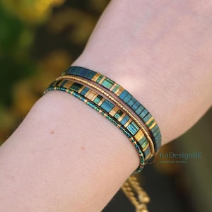May include: Two beaded bracelets in shades of teal, gold, and green are stacked on a wrist. The bracelets feature rectangular and round beads. The bracelets are handmade jewelry.