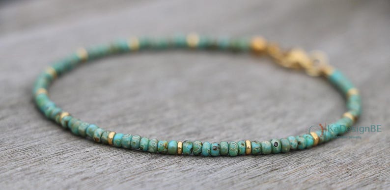 K&ouml;nnte beinhalten: Ein t&uuml;rkisfarbenes und goldenes Perlenarmband mit einem Verschluss. Das Armband besteht aus kleinen, runden Perlen und wirkt zart.