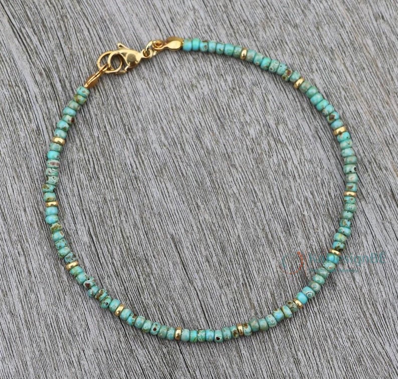 K&ouml;nnte beinhalten: Ein t&uuml;rkisfarbenes und goldenes Armband mit einem goldenen Verschluss.