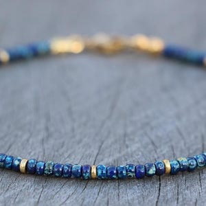 May include: A delicate bracelet featuring small, round, blue and gold beads. The beads are strung together with a gold clasp. The bracelet is a beautiful piece of jewelry.
