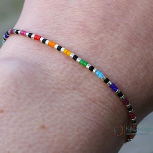 May include: A colorful beaded bracelet with black and silver beads. The bracelet is on a person's wrist.