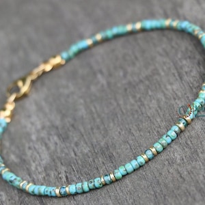 May include: A turquoise and gold beaded bracelet with a lobster clasp closure. The bracelet is made with small, round beads and is approximately 7 inches in length.