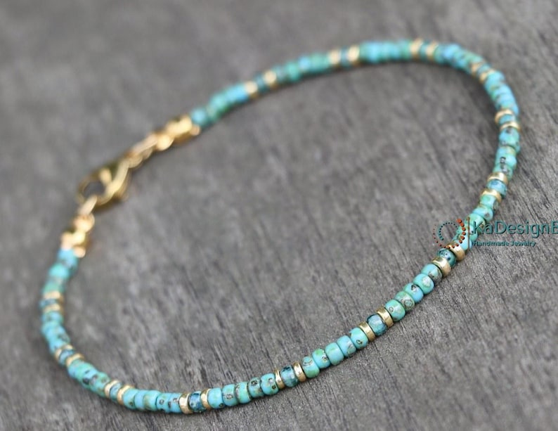 May include: A turquoise and gold beaded bracelet with a lobster clasp closure. The bracelet is made with small, round beads and is approximately 7 inches in length.