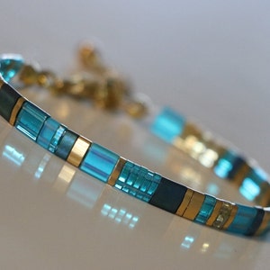tila bracelet close up, flats square beads in aqua, gold, blueish beads in random pattern.