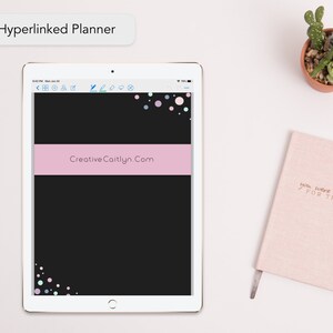Può includere: Un tablet bianco con uno schermo nero che mostra un planner digitale rosa e nero con il testo "CreativeCaitlyn.com" e un design di coriandoli colorati. Il tablet è su una superficie bianca con un quaderno rosa e una pianta grassa in vaso.
