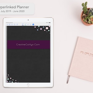 Può includere: Un planner digitale in bianco e nero con uno striscione viola che dice "CreativeCaitlyn.Com". Il planner è aperto sullo schermo di un tablet e ha un design a coriandoli colorati sulla copertina.