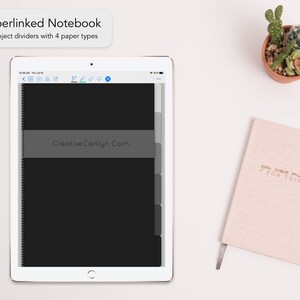 May include: A white tablet computer with a black screen displaying a digital notebook with the text "Creative Caitlyn.com". The tablet is on a white surface next to a pink notebook with the text "you were made FOR THIS" in gold lettering.